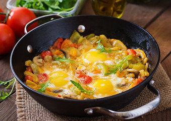 Fried eggs with vegetables in a frying pan on a wooden background