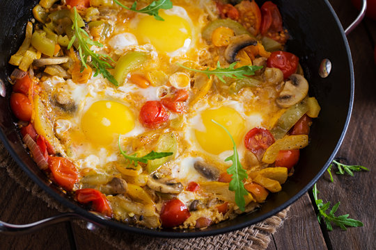 Fried eggs with vegetables in a frying pan on a wooden background