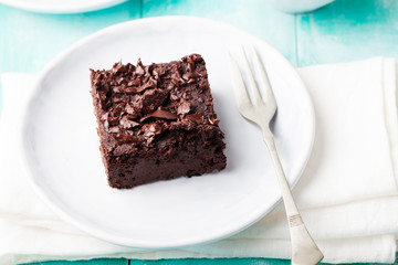 Chocolate brownie, cake, white plate on a turquoise wooden background