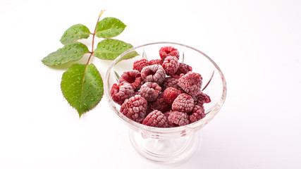 Frozen raspberries in a glass and a green leaf isolated on white background