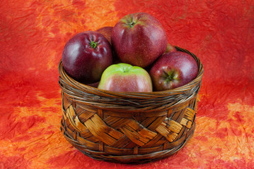 Red delicious apples in wicker basket on yellow and orange background. Autumn concept