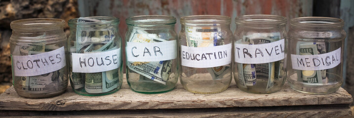Glass jars with dollars and text: house,car, travel, education,clothes, medical.