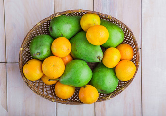 Fresh pears and tangerines in wicker basket on white table