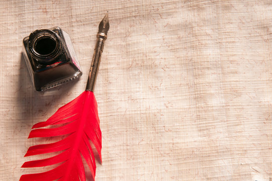 Red quill pen and black inkwell on a papyrus sheet
