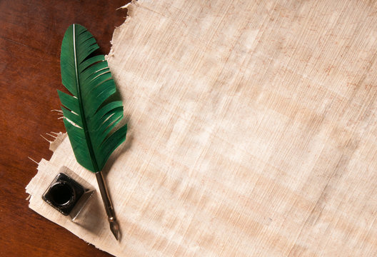 Green quill pen and black inkwell on a papyrus sheet