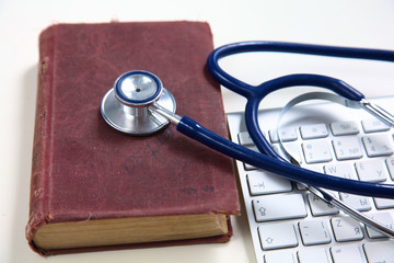 Medical stethoscope with old books and laptop on a table