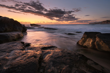Sunrise seascape with rocks and flowing water on long exposure
