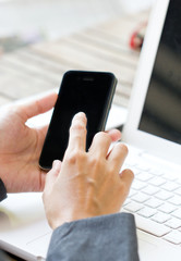 Smartphone in business woman's hands over a white laptop.