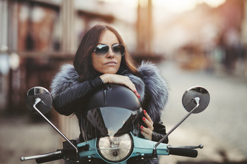 City lifestyle. Cute young woman siting on her Vespa scooter and seriously looking at side....