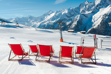 Empty red deck chairs on the snow in a ski resort, Austrian Alps