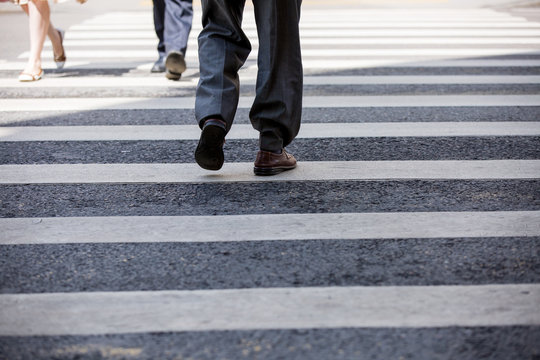 Pedestrian in business suits crossing on the road, feet rushing through the zebra traffic walk way