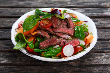 Spicy Beef Slices Meat Salad with Carrots, Tomatoes, Cucumber, Parsley and Salad leaves Spinach, rocket, red ruby chard on old wooden table