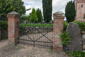 Einfahrt zum Friedhof mit Eisentor und Backsteinpfeilern