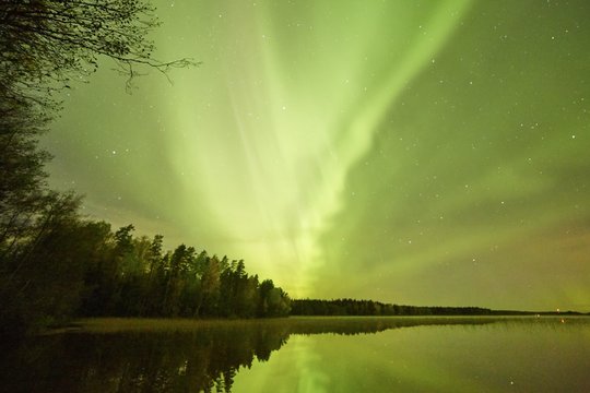 Northern lights (Aurora Borealis) glowing in the night sky over a beautiful lake in Finland. Vibrant colors on the sky and reflections on the still water of the lake.