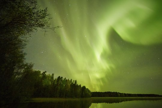 Northern lights (Aurora Borealis) glowing in the night sky over a beautiful lake in Finland. Vibrant colors on the sky and reflections on the still water of the lake.