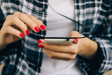 Woman in plaid shirt and red manicure holding white mobile phone