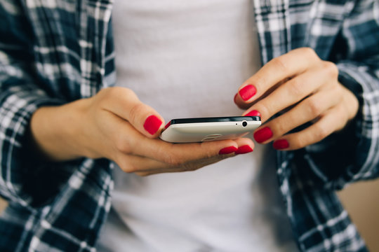 Woman in a plaid shirt and red manicure uses white mobile phone