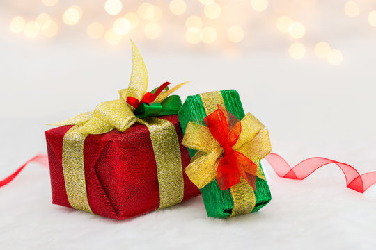 Red and green Christmas gift box with shiny ribbon. Bokeh with glow effect on white background