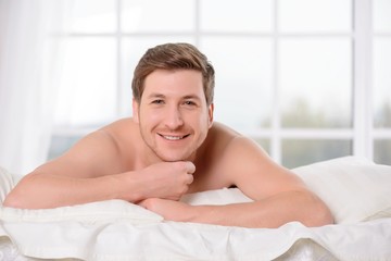 Fototapeta na wymiar Smiling young man lays awake in bed. 