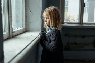 Depressed poot girl standing near window 