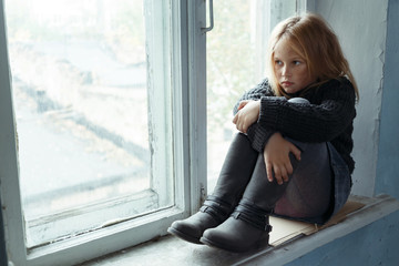 Depressed poot girl standing near window 