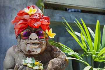 Foto op Canvas Humorous face portrait of old traditional Balinese temple guard statue dressed in funny tourist costume with sunglasses Arts, culture of Bali and Indonesian people and asian vacation travel background © Tropical studio