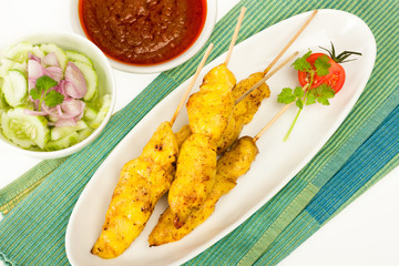 Chicken grilled meat on sticks with cucumber salad on side and chilli sauce