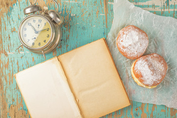 Sweet sugary donuts, book and vintage clock on rustic table