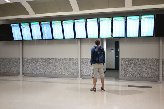 Man is looking and pointing at a departure/arrival board at an airport
