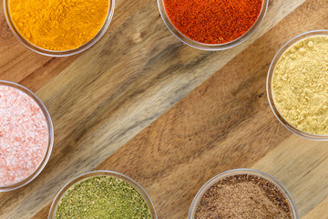 The powders of: bay leaf, turmeric, mustard, red paprika and nutmeg are poured in the glass bowls on the wooden background.