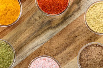 The powders of: bay leaf, turmeric, mustard, red paprika and nutmeg are poured in the glass bowls on the wooden background.
