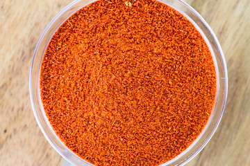 The powder of paprika in the glass bowl on the wooden background.