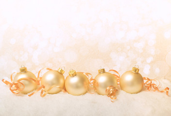 Fototapeta na wymiar Five gold Christmas ornaments with curly ribbon and the message Merry Christmas with bokeh light effects