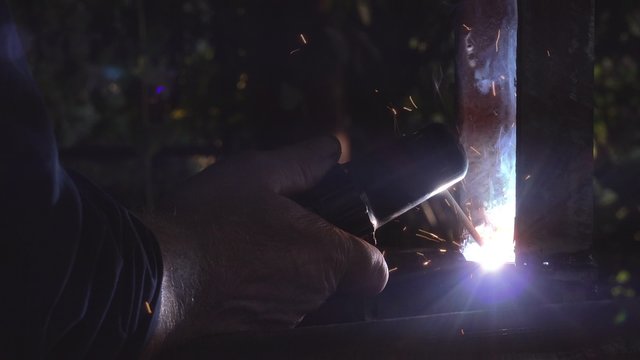 Worker arc welding in workshop, male welder using electrode to melt the metal at the welding point.