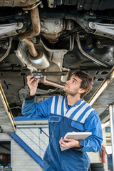 Mechanic Examining Exhaust System Of Car With Flashlight