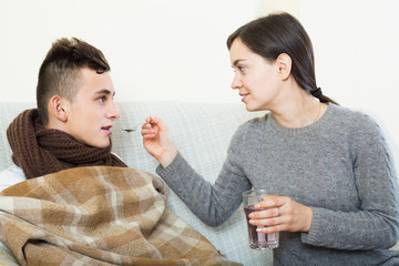 Concerned mother giving mixture to teenage son with cough