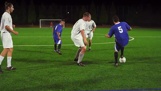 A soccer player dribbles down the field during a game at night

