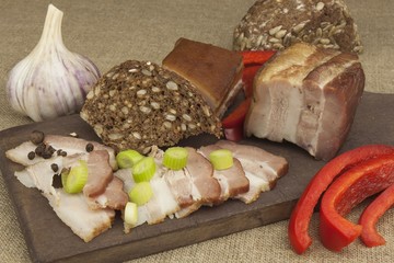 Preparing home-made snacks for the guests. Cutting board with smoked bacon and bread. Raw bacon. Whole grain bread.

