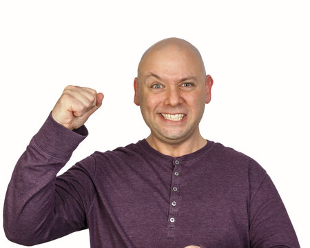 Bald man in studio portrait on white background pumps his fist in the air shows extremely pleased emotion. He is wearing a purple long-sleeved shirt with white buttons, gritting his teeth and smiling.