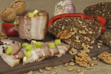 Preparing home-made snacks for the guests. Cutting board with smoked bacon and bread. Raw bacon. Whole grain bread.
