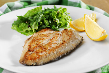 Dish of fish fillet with greens and lemon on plate close up
