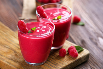 Glasses of raspberry milk shake with berries on wooden table close up