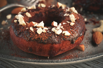 Delicious doughnut with chocolate icing and nuts on plate close up