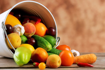 Heap of fresh fruits and vegetables in bucket on wooden table close up