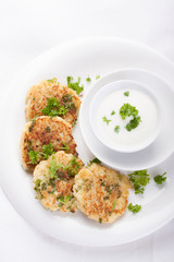 Cabbage pancakes with parsley and yogurt dressing on a white plate. Top view