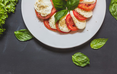 Caprese salad with mozzarella, tomato, basil on white plate. Top