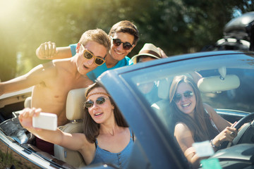 young people taking selfies with a smartphone in convertible