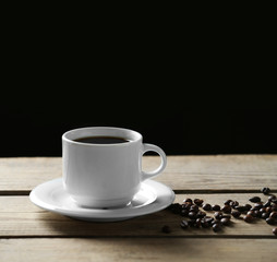 Cup of coffee and coffee grains on wooden table, on gray background