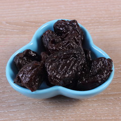 Dried plums in blue bowl on wooden table, healthy food