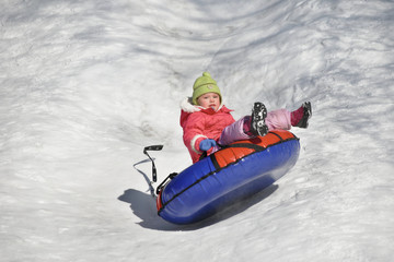 Fototapeta na wymiar A little girl up in the air on a tube sledding in the snow 